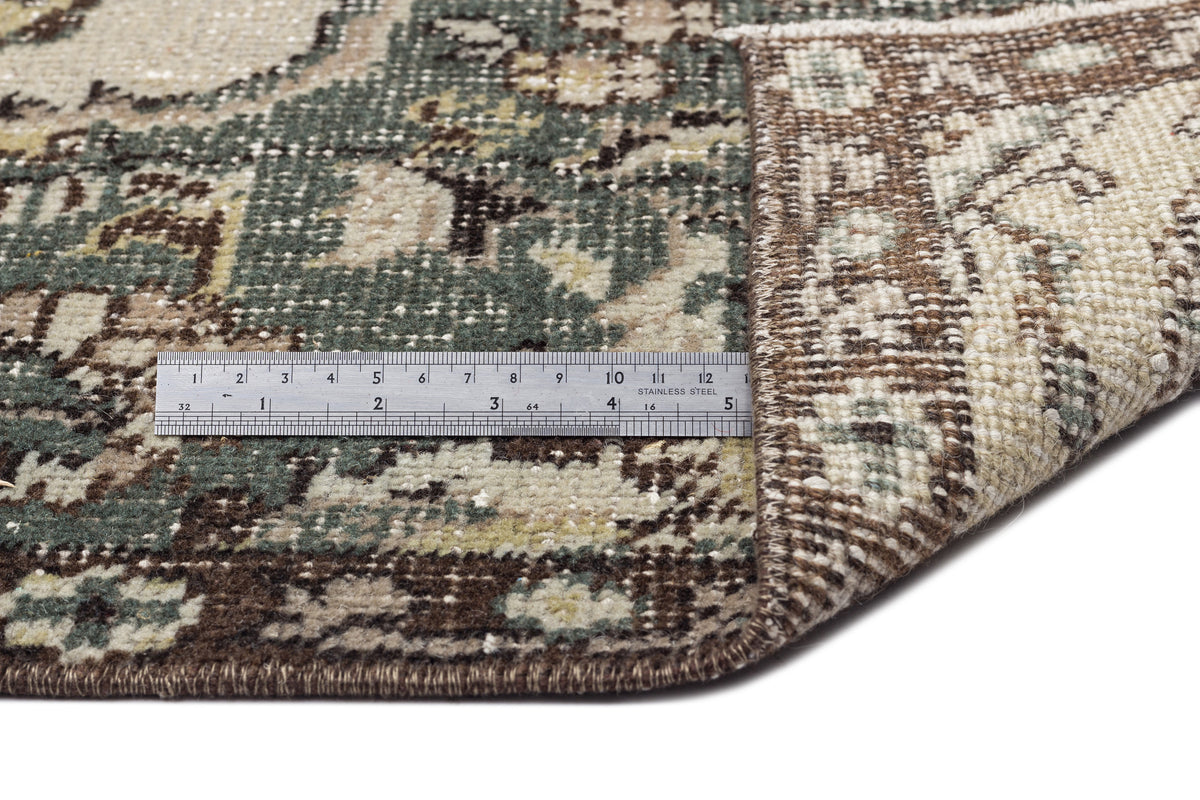 Distressed sage green and brown traditional medallion rug with a metal ruler showing pile height on a white background.