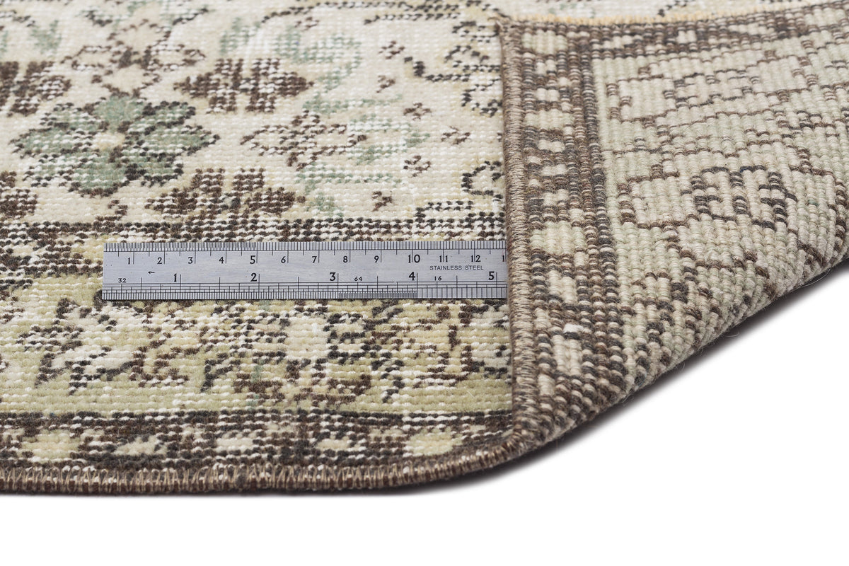 Beige, brown, and sage green floral medallion rug with a folded corner and a metal ruler for scale.