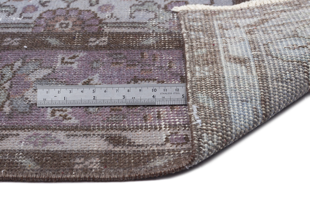 Distressed purple and brown traditional rug with a folded corner revealing the backing, shown with a metal ruler.
