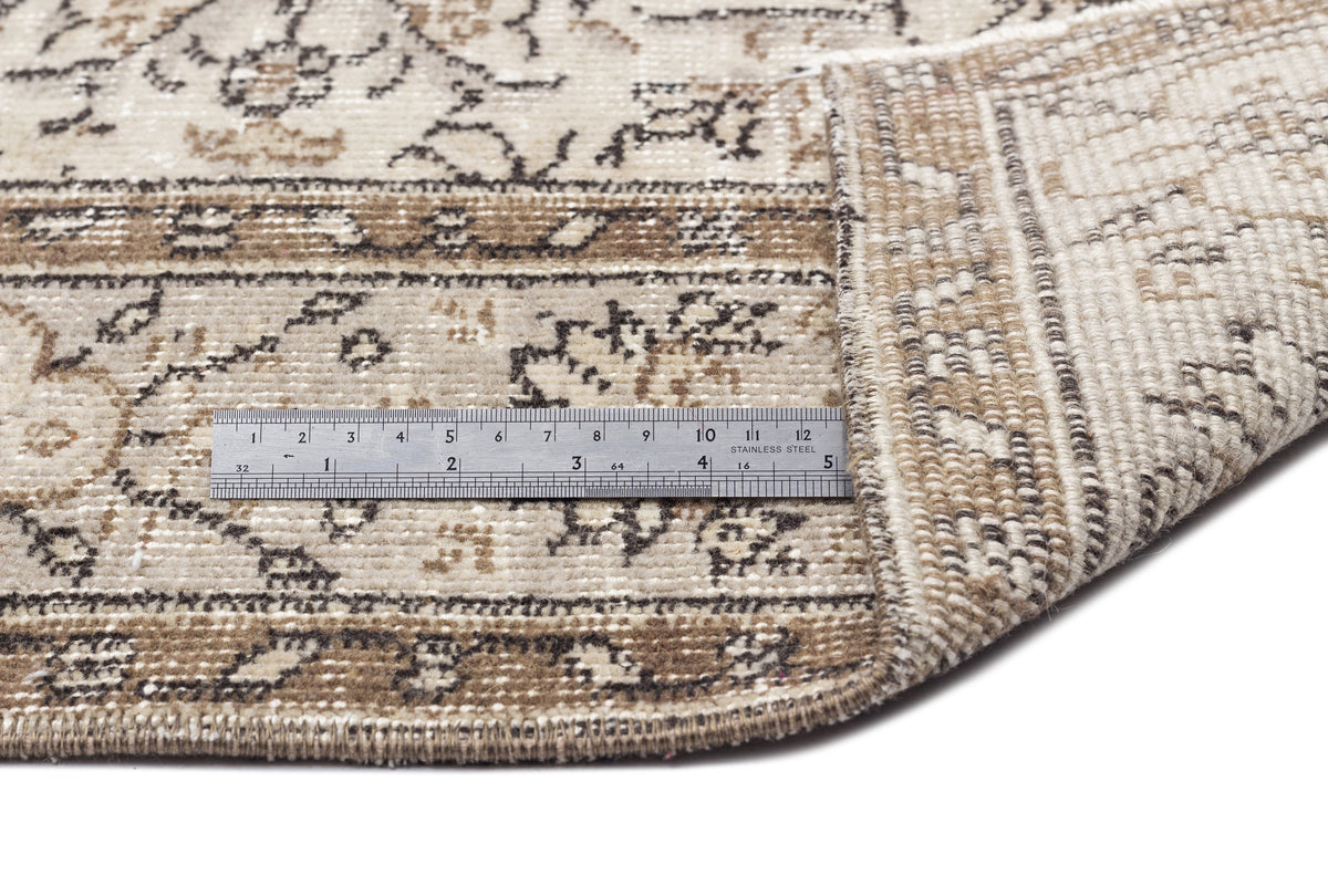 Beige and brown distressed rug with a traditional floral pattern, shown with a metal ruler for scale on a white background.
