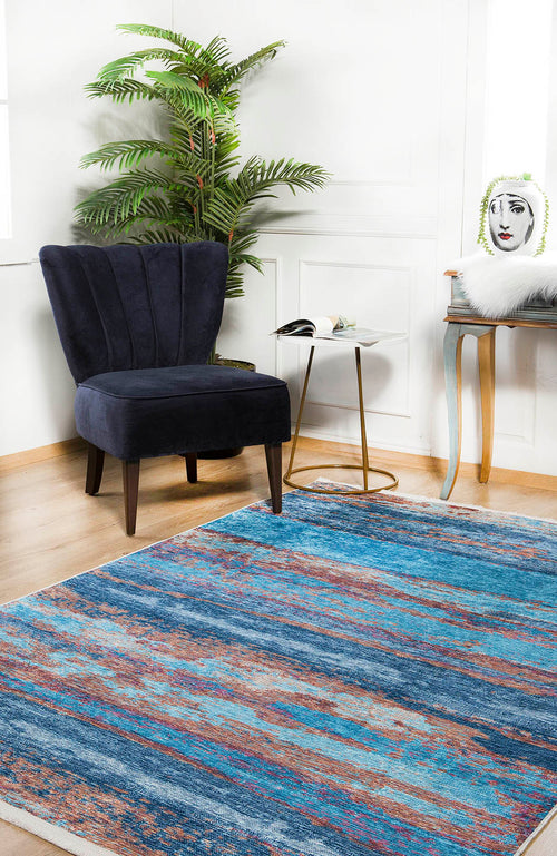 Load image 1 in gallery view. A modern living room with a blue accent chair, round white side table, plant, illustrated face pillow, and the Abstract Elegance - Machine-Washable Rug JR87 (Custom Size) on wood floors. Light pours in through a window.