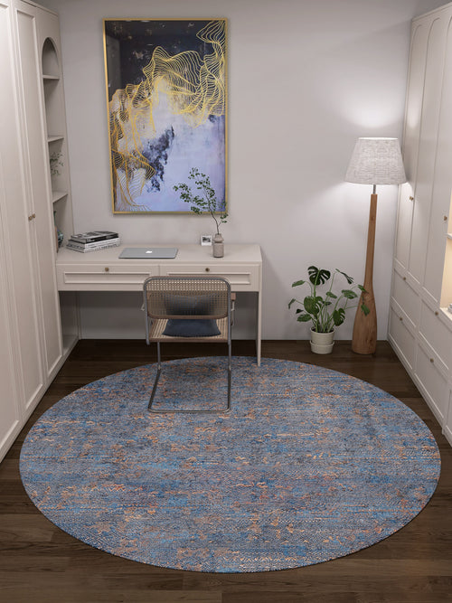 Load image 1 in gallery view. A modern home office features a white desk, rattan chair, and the Abstract Harmony - Machine-Washable Rug JR1882 (Custom Size)—ideal for high-traffic areas. A tall lamp and plant stand right; gold and blue abstract art hangs above built-in white shelves.