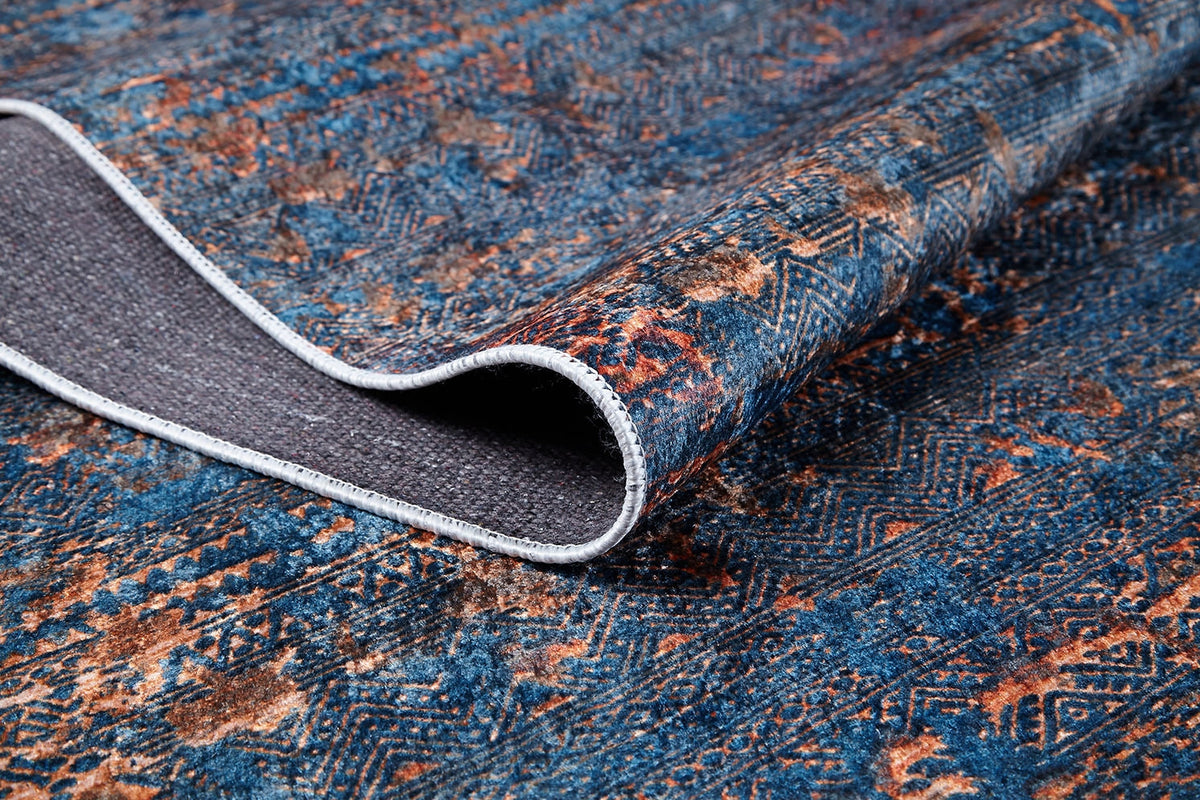 A close-up of the Abstract Harmony - Machine-Washable Rug JR1882 (Custom Size), showing its blue and orange pattern with one corner lifted to display the textured gray underside—ideal for high-traffic areas and highlighting its intricate woven detail.