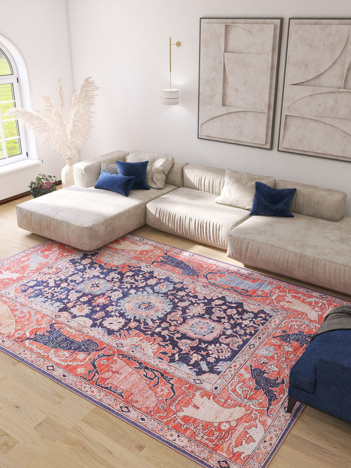 A bright living room with a large beige sectional, blue accent pillows, light wood floors, abstract wall art, and an Aegis Handmade-Design Washable Rug - LCC3029 (Custom Size) ideal for high-traffic areas beside a tall vase of pampas grass near a window.