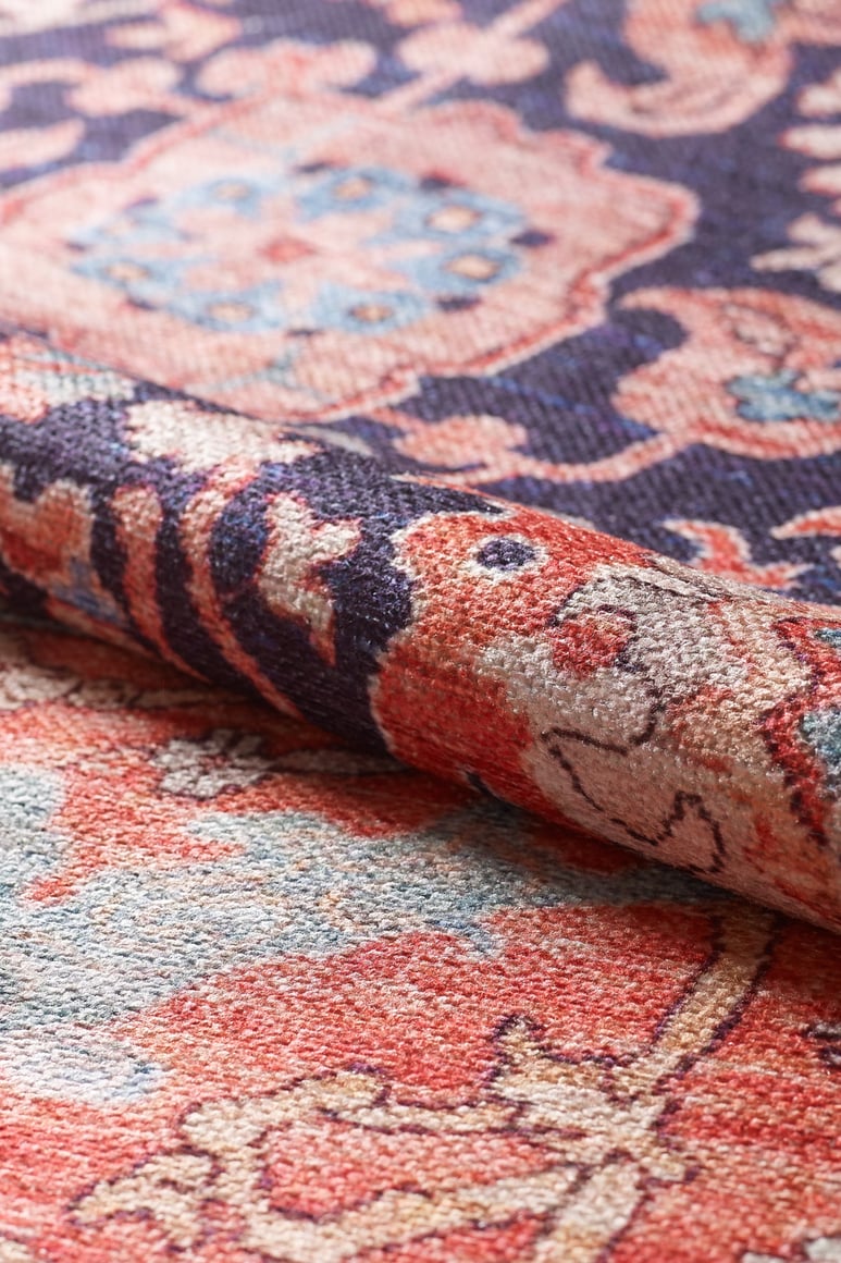 A close-up of the Aegis Handmade-Design Washable Rug - LCC3029 (Custom Size), rolled to highlight its fine texture and detailed red, blue, pink, and cream patterns—an ideal choice for allergy-sensitive homes.