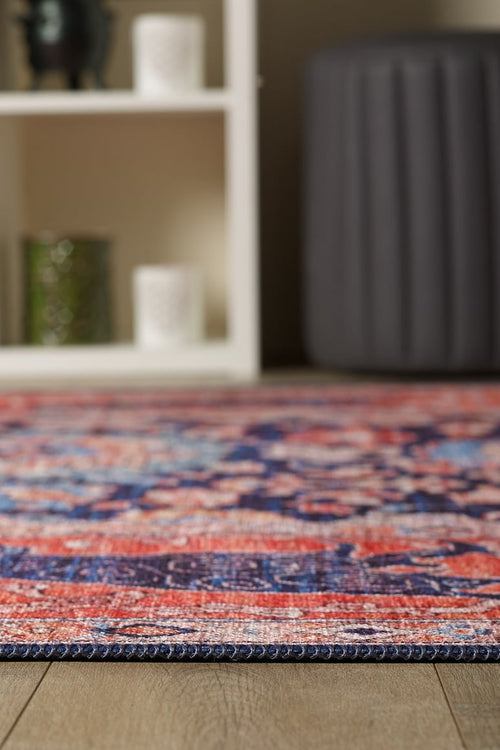Load image 1 in gallery view. A close-up of the Aegis Handmade-Design Washable Rug - LCC3029 (Custom Size) with vibrant red, blue, and pink patterns on a wooden floor—perfect for allergy-sensitive homes. A white shelf and dark gray ottoman are in the background.