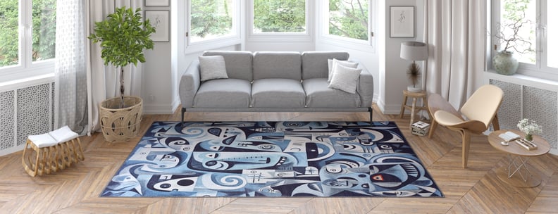 A modern living room with a gray sofa, light wood furniture, large windows, potted plant, and the Aesthetic Anomaly Contemporary Washable Rug - MDJ004 in blue with abstract patterns—ideal for high-traffic areas—on a herringbone wood floor.