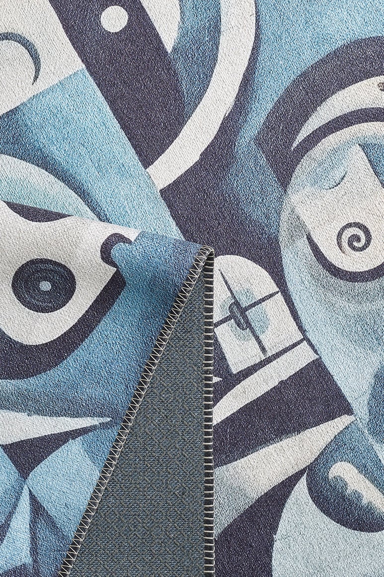 A close-up of the Aesthetic Anomaly Contemporary Washable Rug - MDJ004 (Custom Size) shows its blue, black, and white abstract face design. One corner is folded to reveal the stitched edge and reverse pattern—great for high-traffic areas.