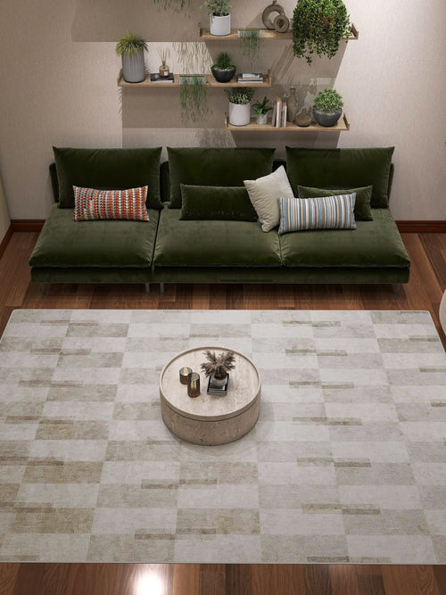 Bild 1 in Galerieansicht laden. A modern living room featuring a green velvet sofa, assorted pillows, a round coffee table with decor, the Aged Elegance - Washable Rug - JRN37 ideal for high-traffic areas, plus shelves displaying potted plants and books on a beige wall.