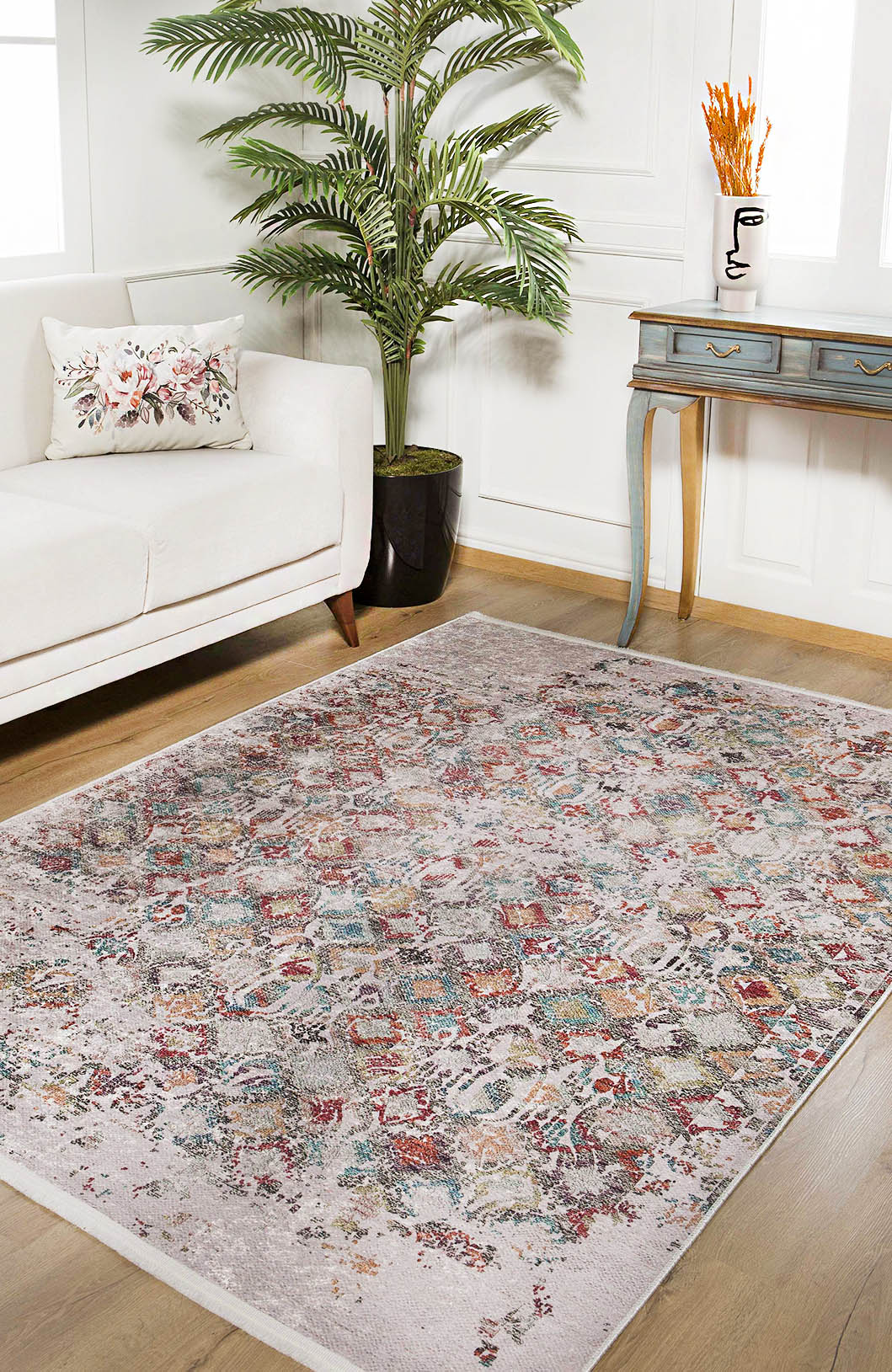 A stylish living room with the Aged Mosaic - Washable Rug - JR1096 (Custom Size) on wood floors, a white sofa with a floral pillow, potted plant, and blue vintage console table with an abstract vase—perfect for high-traffic areas.