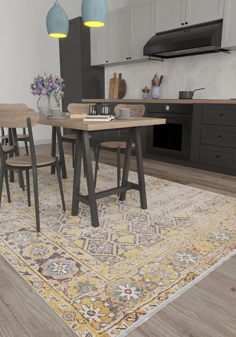 Modern kitchen with light wood table and chairs on the Aged Splendor - Washable Rug - JR1906 in yellow-gold, ideal for high-traffic areas. Black cabinets, blue hanging lights, and neutral walls complete the space.