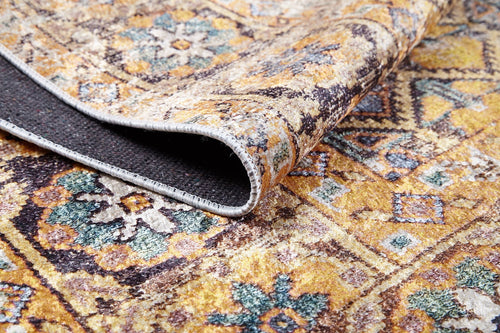 Bild 1 in Galerieansicht laden. A close-up of the Aged Splendor - Washable Rug - JR1906 (Custom Size) in yellow-gold, brown, and blue earthy tones, with a folded edge revealing its dark underside and fine stitching—ideal for high-traffic areas.