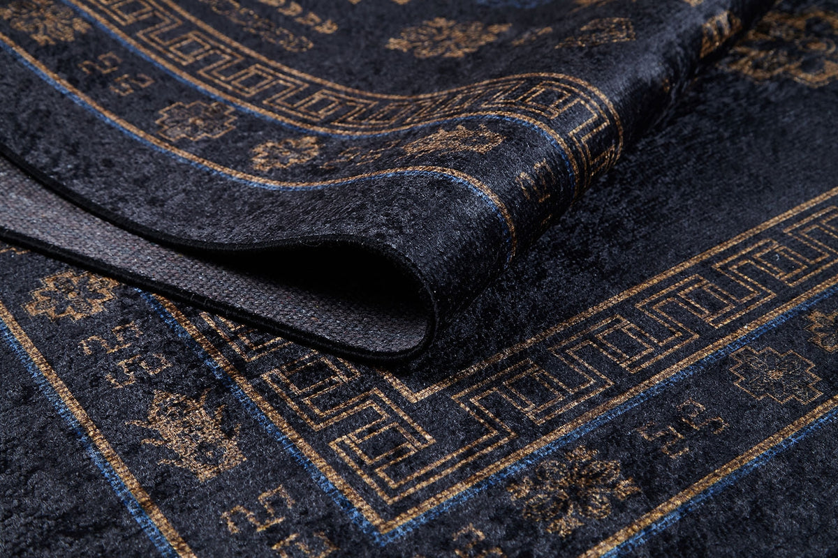 Close-up of the Ancient Legacy - Washable Rug - JR1890 (Custom Size) in dark blue and gold, featuring geometric and floral patterns. A folded corner reveals the rug's thickness and textured flat weave material.