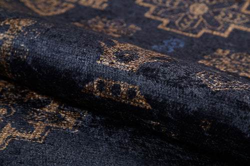 Load image 1 in gallery view. A close-up of the Ancient Legacy - Washable Rug - JR1890 (Custom Size) shows its velvety black surface with gold geometric and floral patterns, partially rolled to display the flat weave texture and detailed design.
