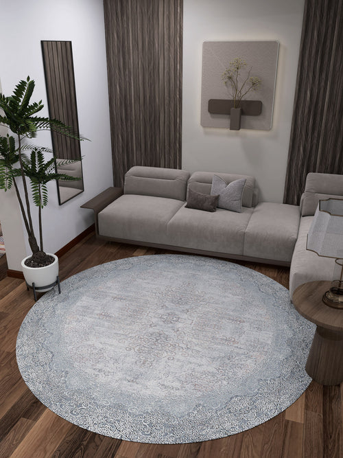 Load image 1 in gallery view. A modern living room features a gray sectional sofa, the Ancient Treasure - Washable Rug - JR1785 (Custom Size) in blue—ideal for high-traffic areas—a potted plant, wood panel walls, a small side table, and minimalist wall art above the couch.