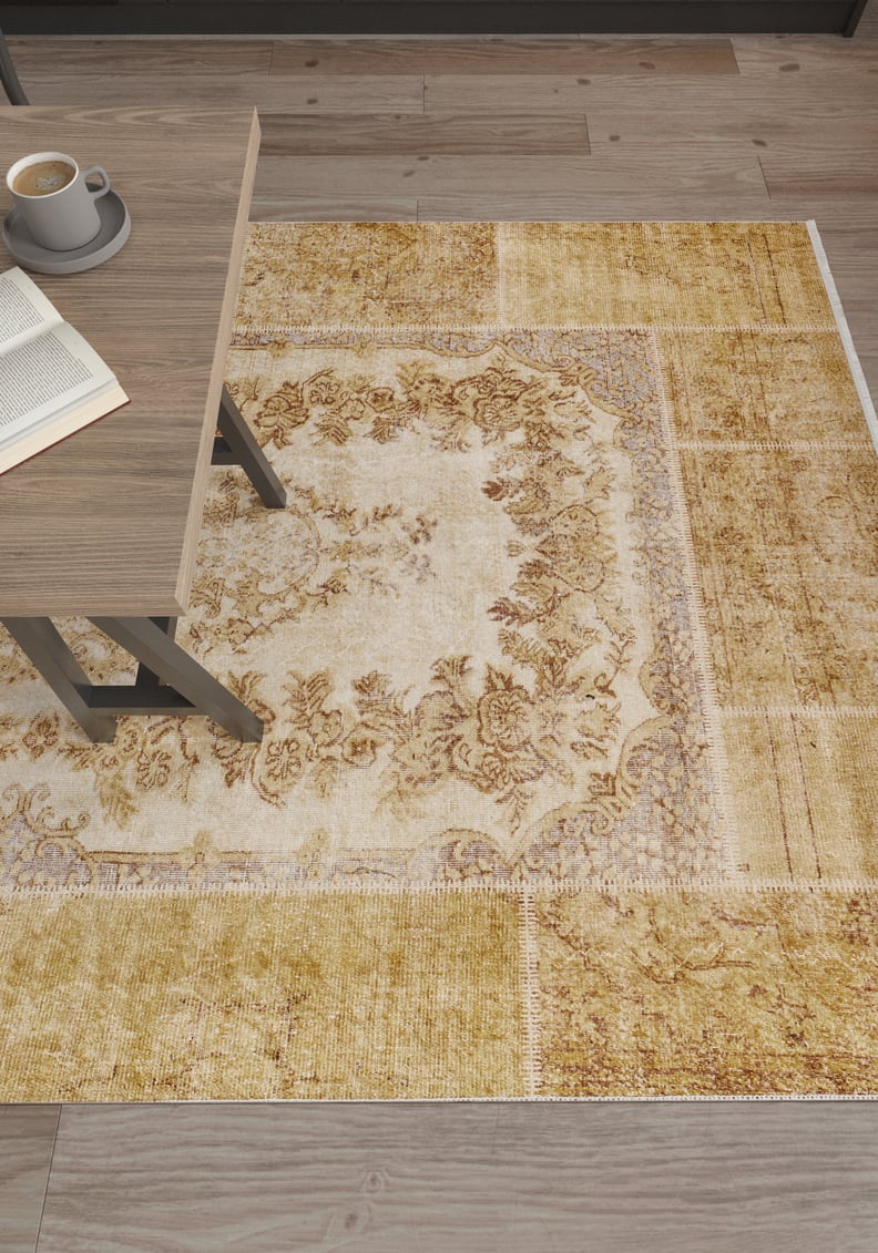 A wooden table with an open book and coffee sits atop the Antique Insignia - Washable Rug - JR309, featuring yellow-gold florals—perfect for high-traffic areas—on a wooden floor.