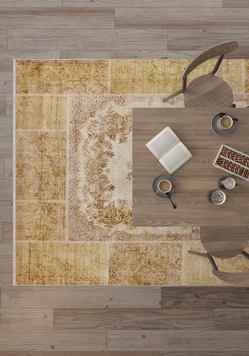 Load image 1 in gallery view. Top-down view of a wooden table with two chairs, coffee cups, an open book, and snacks atop the Antique Insignia - Washable Rug - JR309 in yellow-gold tones over a wooden floor.