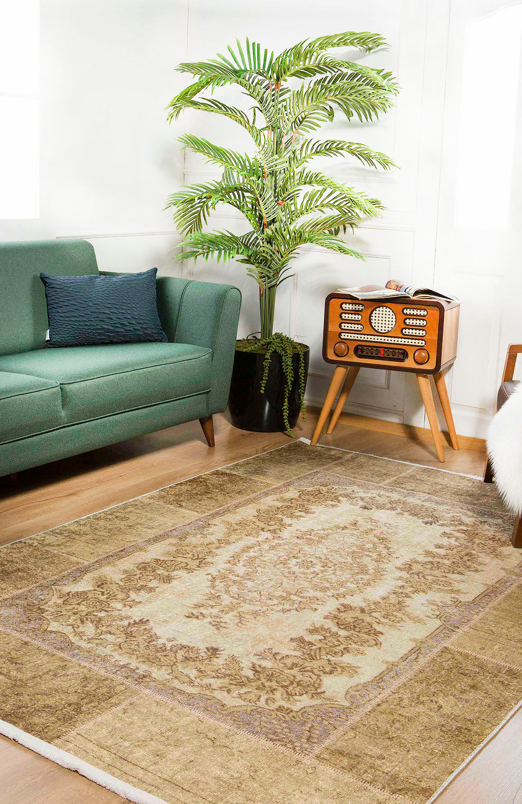 A cozy living room with a green sofa, vintage radio on a wooden stand, tall potted palm, and the Antique Insignia - Washable Rug - JR309 (Custom Size) in beige and brown—perfect for high-traffic wooden floors.