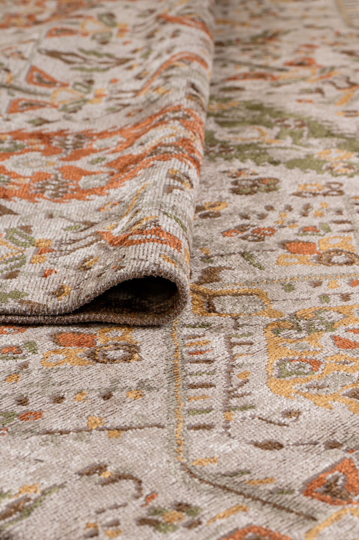 A close-up of the Saffron Heritage Area Rug APX1912 shows its intricate, colorful pattern in orange, green, and gold on a beige background. The texture and flatwoven construction are clearly visible.