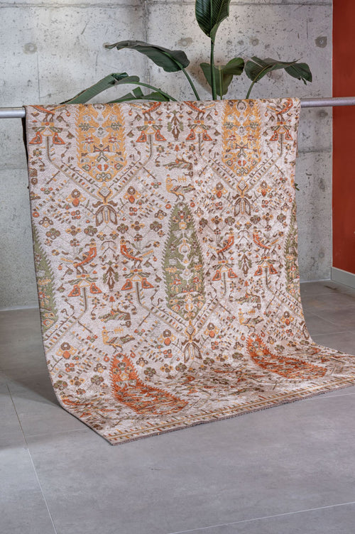 Load image 1 in gallery view. The Saffron Heritage Area Rug APX1912, featuring earthy tones and intricate motifs in a flatwoven design, hangs over a metal railing in a modern room with a concrete wall, gray tiled floor, and a tall leafy plant.