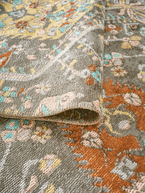 Load image 1 in gallery view. Grey rug with a distressed floral medallion pattern in orange, yellow, and turquoise, shown with a folded corner.