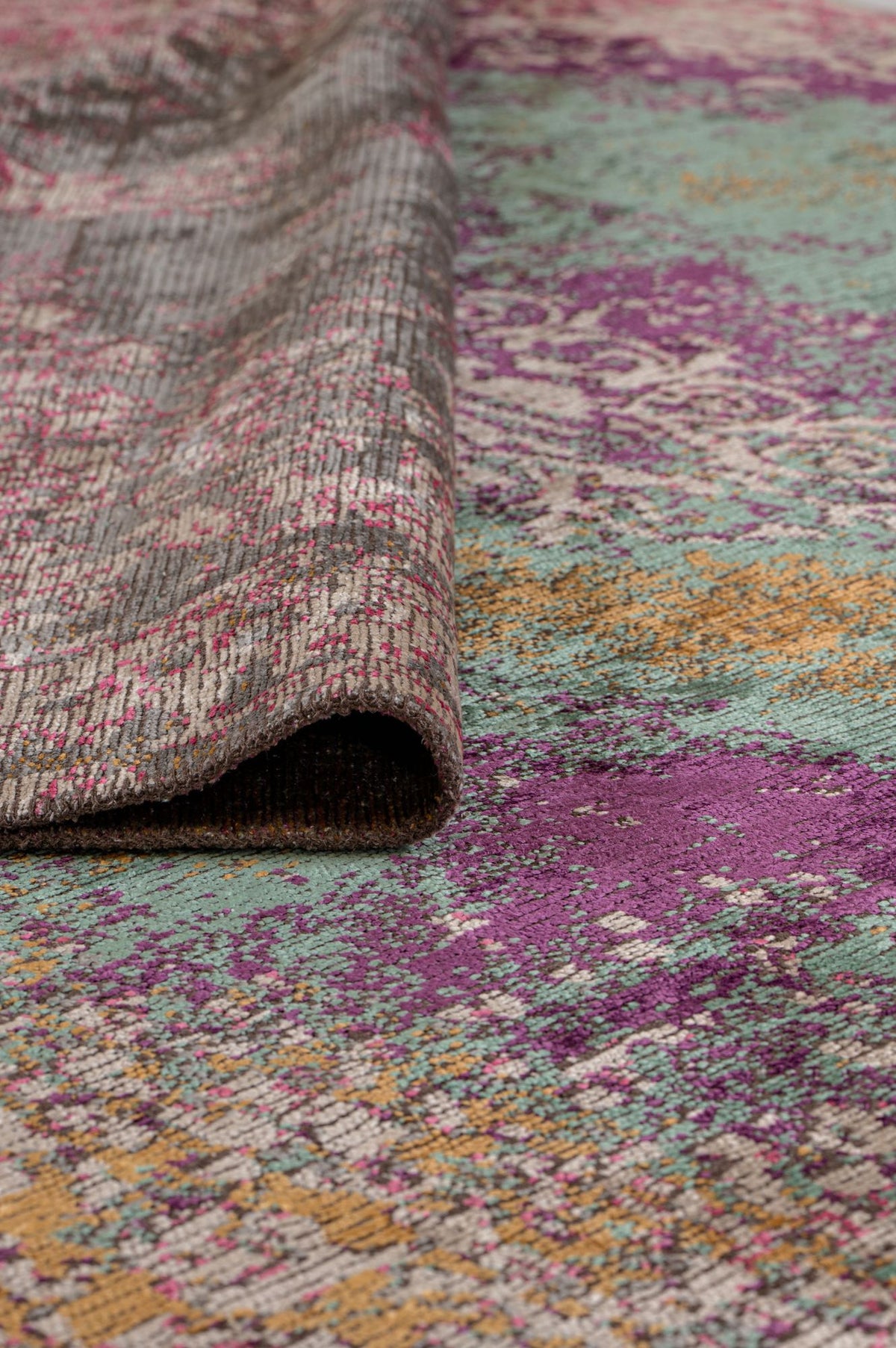 Distressed purple, teal, and gold abstract patterned rug with a curled corner showing the textured backing.