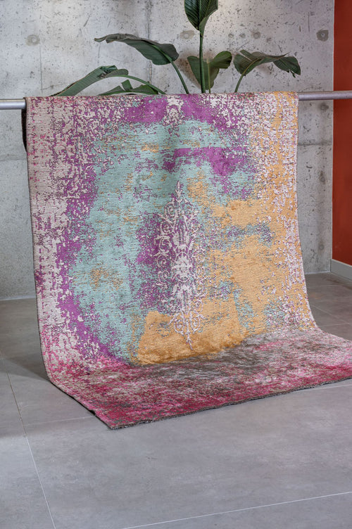 Load image 1 in gallery view. Distressed abstract rug in magenta, teal, and gold with a faded central medallion, draped against a concrete wall.