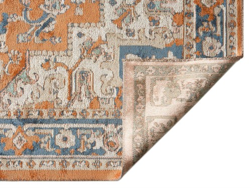 Load image 1 in gallery view. Distressed orange, blue, and cream traditional rug with a floral medallion pattern, shown with a corner folded over.