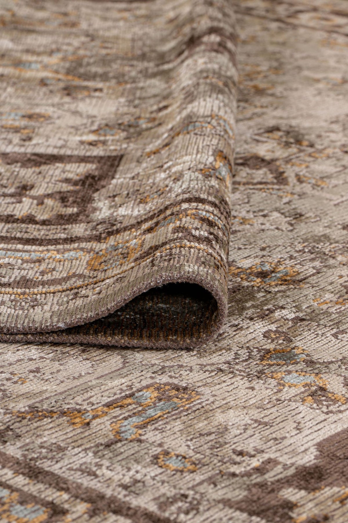 A close-up of the Ivory Medallion Area Rug APX1932 in neutral tones with blue and gold highlights, partially folded to reveal its thickness, medallion motif, and rich texture.