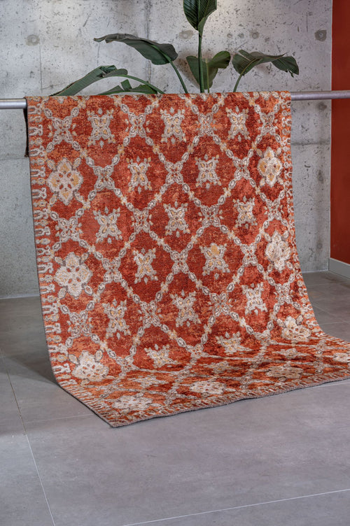 Load image 1 in gallery view. Rust-colored rug with a cream diamond lattice and floral medallion pattern, draped over a bar in a studio setting.