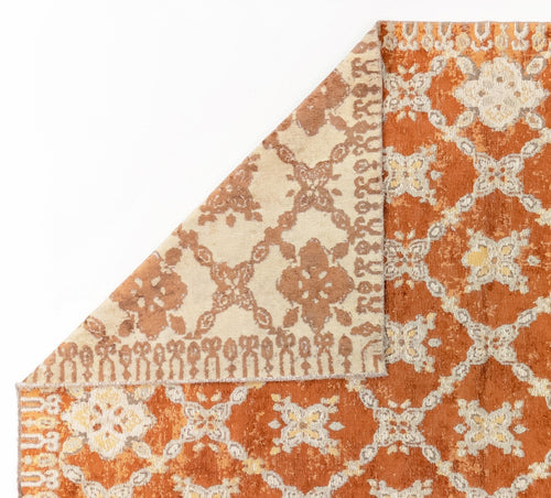 Load image 1 in gallery view. Rust and cream rug with a distressed floral trellis pattern, shown with a corner folded over to reveal the reverse side.