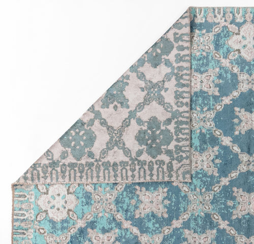 Load image 1 in gallery view. The Ocean Trellis Area Rug APX1942 is a modern flatwoven rug in blue and gray, featuring floral and geometric motifs in turquoise, teal, and gray. One corner is partially folded to reveal the underside.
