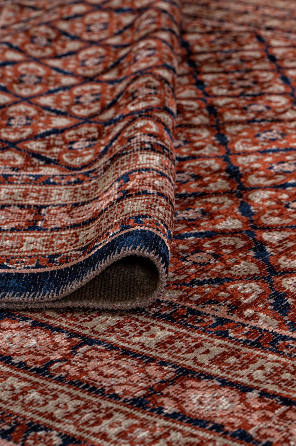 Rust, navy, and beige rug with a repeating geometric diamond pattern, shown folded to reveal the woven backing.