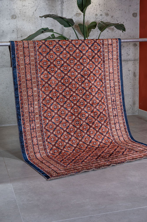 Load image 1 in gallery view. Rust and navy blue rug with a geometric diamond lattice pattern, draped over a metal bar in a studio setting.