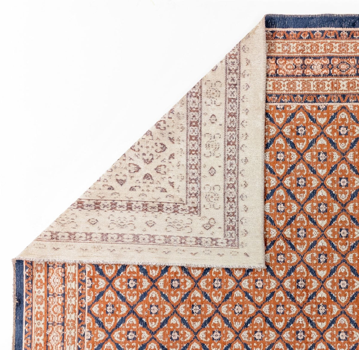 Rust and navy blue rug with a geometric diamond pattern, shown with a corner folded to reveal the cream-colored backing.