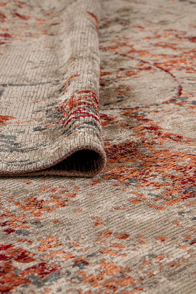 Beige rug with a distressed abstract pattern in rust orange and charcoal grey, showing a folded corner texture.