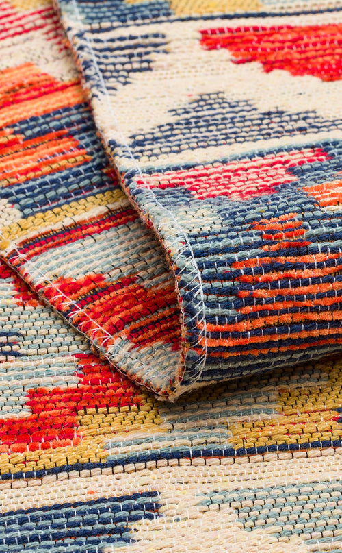 Bild 1 in Galerieansicht laden. A detailed view of the Aqua Flow - Washable Reversible Kilim - NMD02 shows its vibrant red, blue, yellow, and cream patterns. The folded corner highlights the textured weave and striking geometric designs of this unique area rug.
