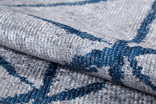 Load image 1 in gallery view. Close-up of the Arabesque Trellis - Washable Rug - JR1732 (Custom Size) in textured gray with blue geometric lines, highlighting its weave and folded fabric—perfect for high-traffic areas.