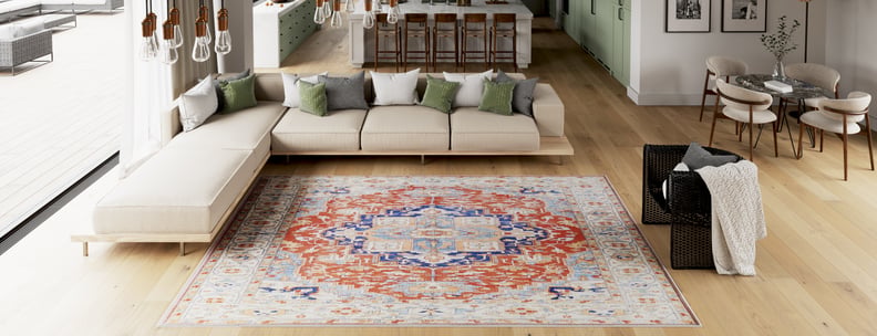 Modern open-plan living room with light wood floors, a large beige sectional sofa, green and white throw pillows, the Ardentis Medallion Washable Rug - LCC3002 (Custom Size) in red multicolor, and a kitchen in the background.