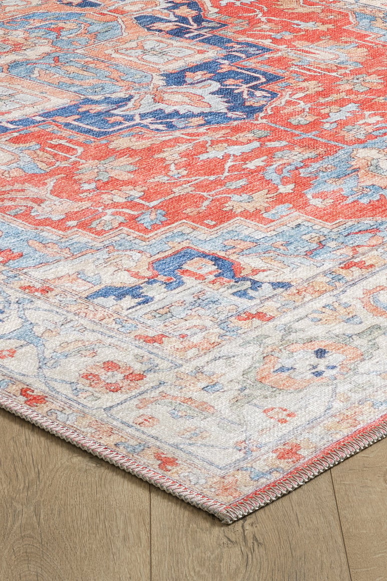 A close-up of the Ardentis Medallion Washable Rug - LCC3002 (Custom Size) showcases its vibrant red, blue, and cream patterns and detailed flat weave texture on a wooden floor.