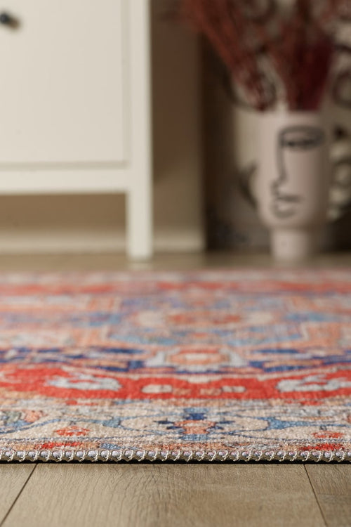 Load image 1 in gallery view. Close-up of the Ardentis Medallion Washable Rug - LCC3002 (Custom Size) in red multicolor on a wooden floor, with a white cabinet and a face-design vase softly blurred in the background.