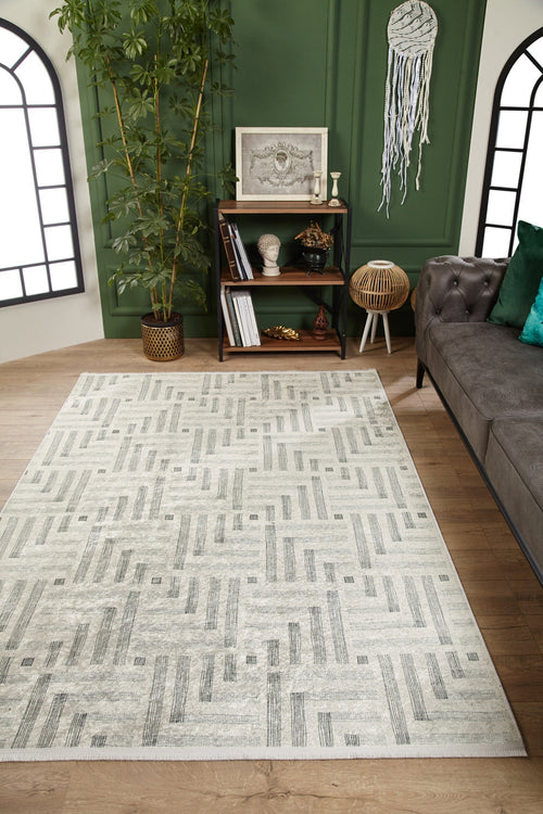 Load image 1 in gallery view. A modern living room features the Art Deco Chic - Washable Rug - JR1832 (Custom Size) in cream and beige—ideal for high-traffic areas—paired with a green wall, black bookshelf, potted plant, gray sofa with green pillows, and arched windows.