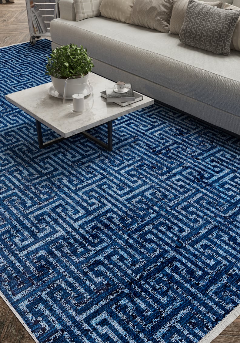 A modern living room features a white sofa, gray and white cushions, a marble coffee table with a plant and tray, and the Art Deco Elegance - Washable Rug - JR1224 (Custom Size) in blue geometric pattern on the wooden floor.