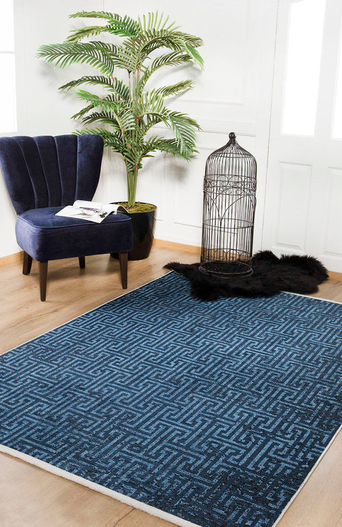 Load image 1 in gallery view. A modern room features the Art Deco Elegance - Washable Rug - JR1224 (Custom Size), a navy velvet chair with a book and glasses, a potted plant, black faux fur rug, and empty birdcage—ideal for high-traffic areas.