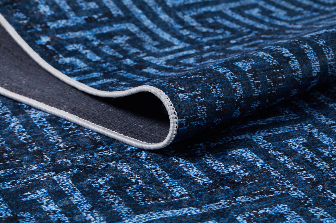 A close-up of the Art Deco Elegance - Washable Rug - JR1224 (Custom Size) in blue shows its geometric design, folded corner with dark underside, and a light-stitched edge—ideal for high-traffic areas.