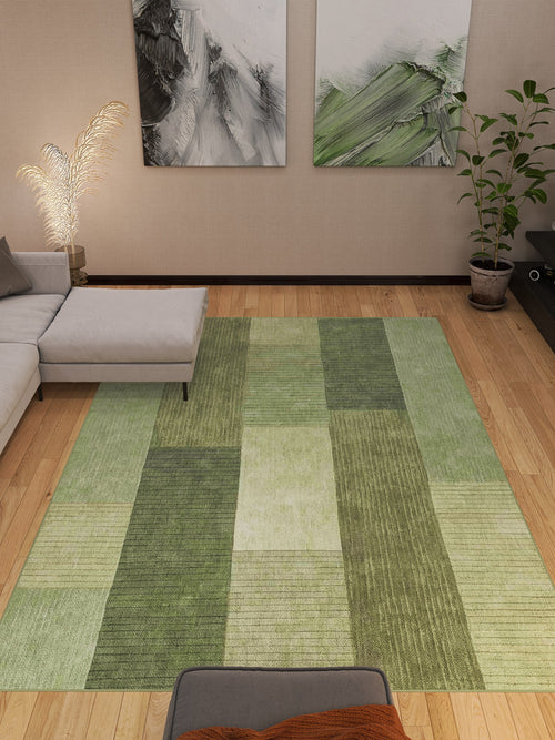 Bild 1 in Galerieansicht laden. A modern living room with the Artisanal Essence - Washable Rug - JRN32 in green patchwork on a wooden floor, a gray sectional, potted plant, wall art, and a feathery floor lamp—ideal for high-traffic spaces.