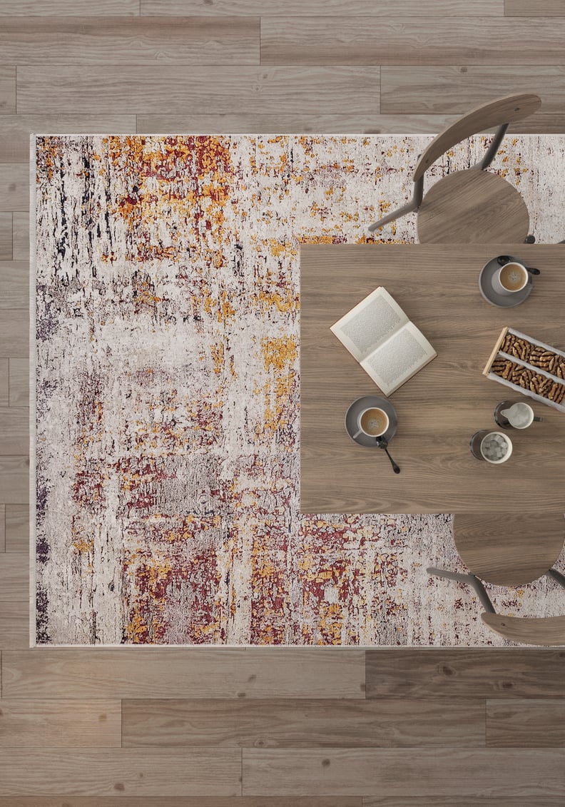 A top-down view of a wooden table with two chairs, two cups of coffee, an open book, and biscuits sits atop the Artistic Abstraction - Washable Rug - JR775, an allergy-friendly flat weave rug with a colorful abstract pattern over wooden flooring.