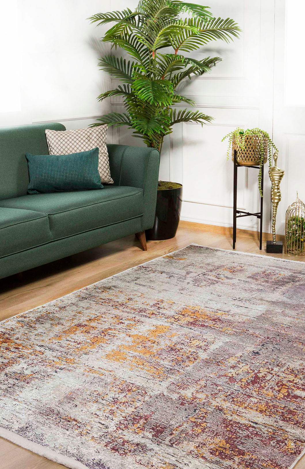 A modern living room features a green sofa with patterned cushions, a large potted plant, and the Artistic Abstraction - Washable Rug - JR775 (Custom Size) on a wood floor. In the corner, a small black stand holds plants and gold lanterns.