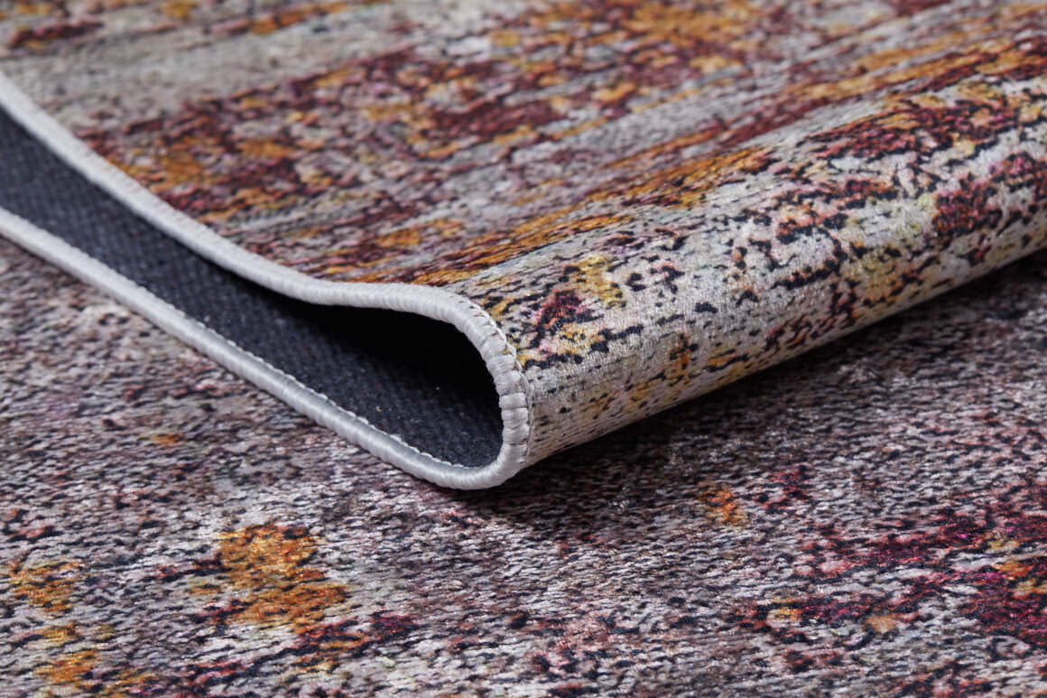 A close-up of the Artistic Abstraction - Washable Rug - JR775 (Custom Size) features a multicolored flat weave with a folded corner, displaying textured gray, yellow, and red patterns and a white stitched edge.
