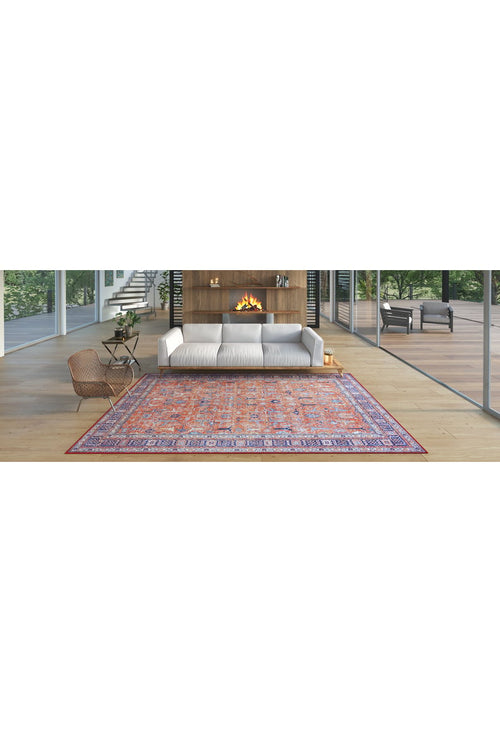Load image 1 in gallery view. A modern living room with a white sofa, wood-paneled fireplace, Aurelius Coral Washable Rug - LCC3005 featuring colorful patterns, a wicker chair, and large glass windows overlooking greenery and a patio—ideal for high-traffic areas.
